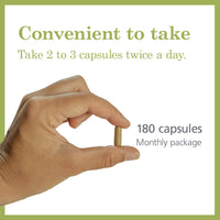 Hand holding a single MAAX Boost capsule with text indicating dosage recommendation of 2 to 3 capsules twice a day and a monthly package of 180 capsules.
